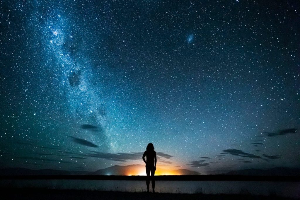 New zealand, canterbury, twizel, silhouette of man looking at lake poaka under starry sky